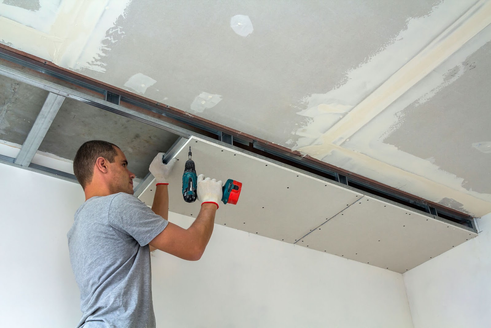Man drilling dryall onto his ceiling