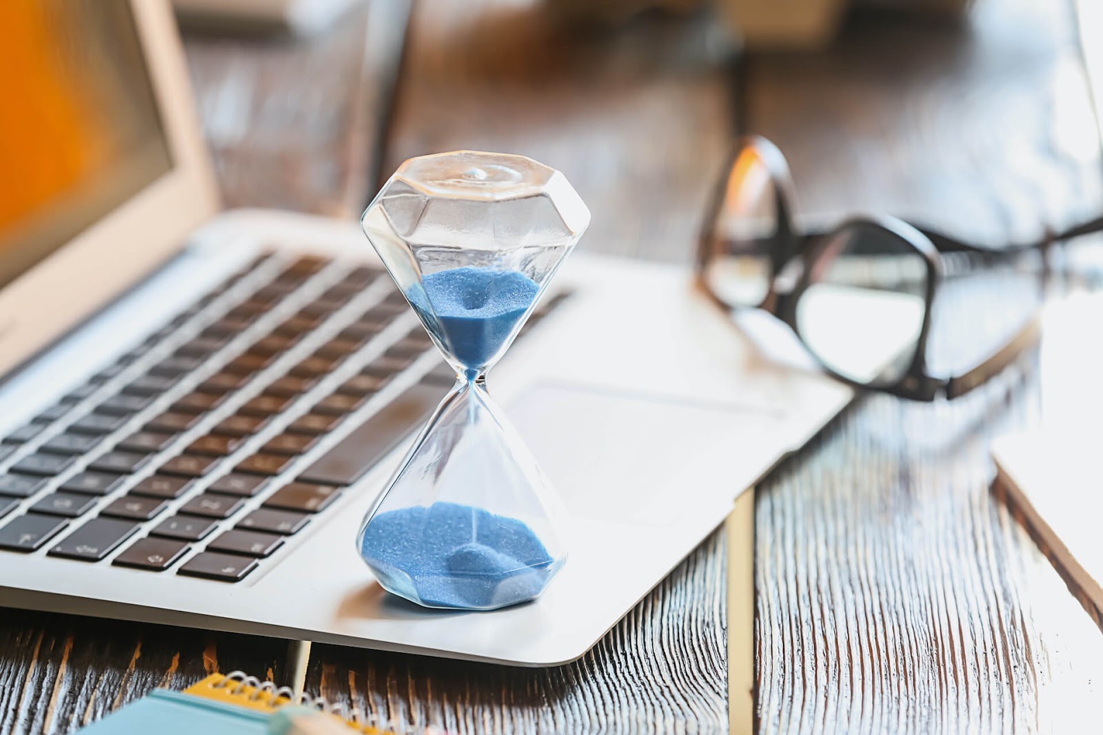 Hourglass on a laptop with glasses in the background