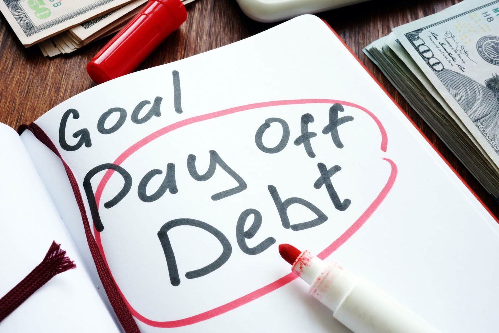 "Pay off debt" written in a goal book with some money laying around it