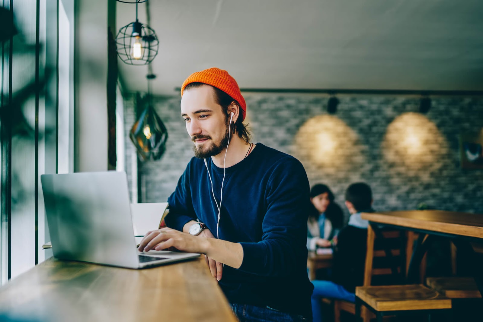 Man working on his laptop in a coffee shop with headphones in