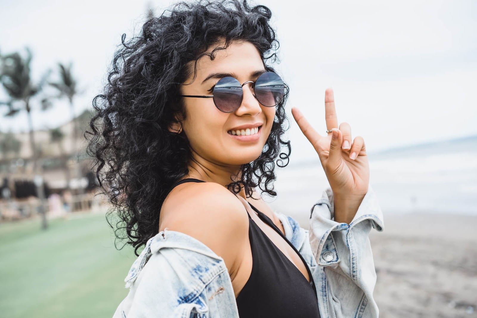 Curly haired, trendy woman giving a peace sign to the camera