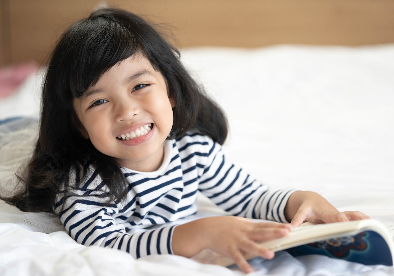 Young asian girl smiling on a bed with her book
