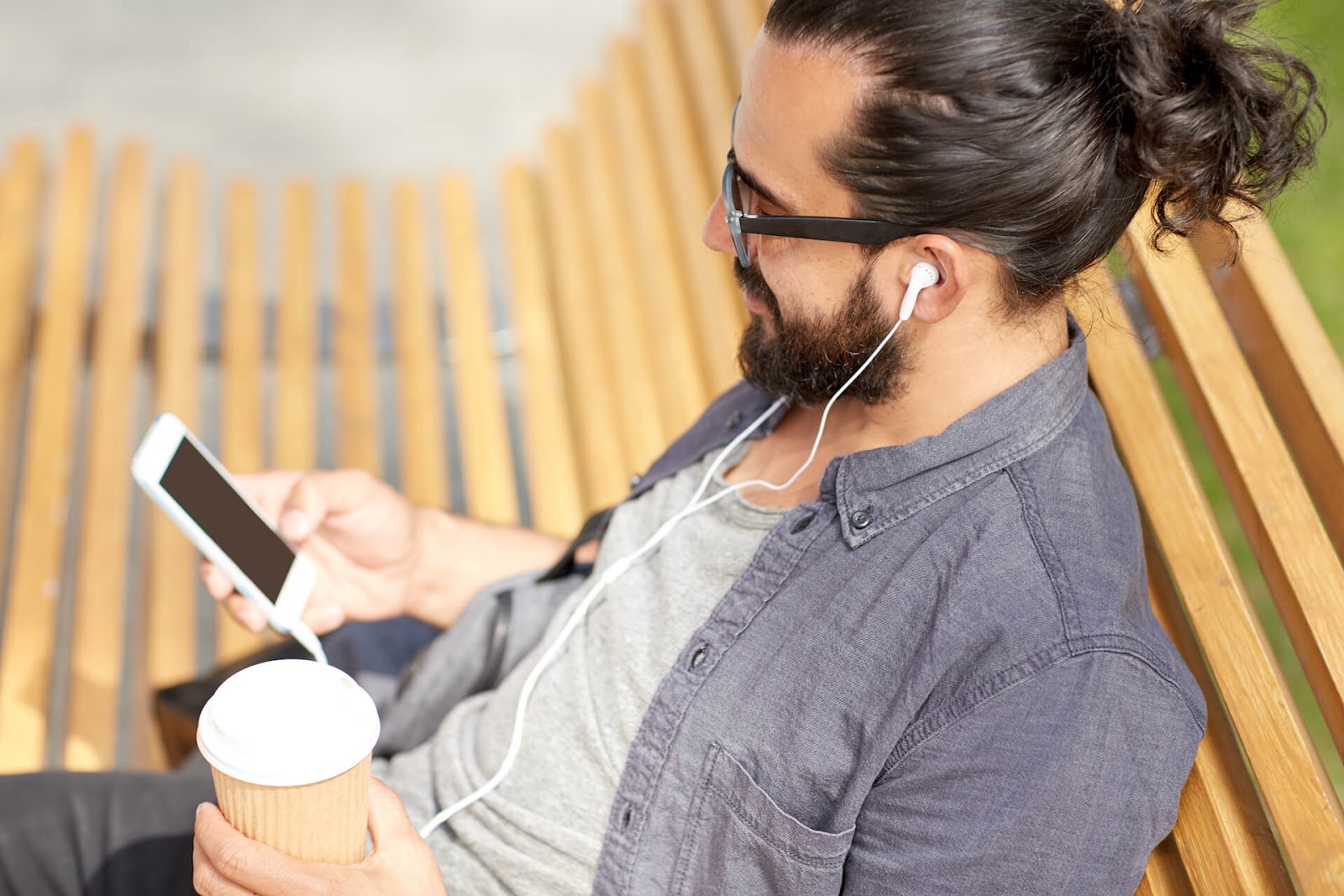 Man sitting on a bench with his headphones, looking at his phone