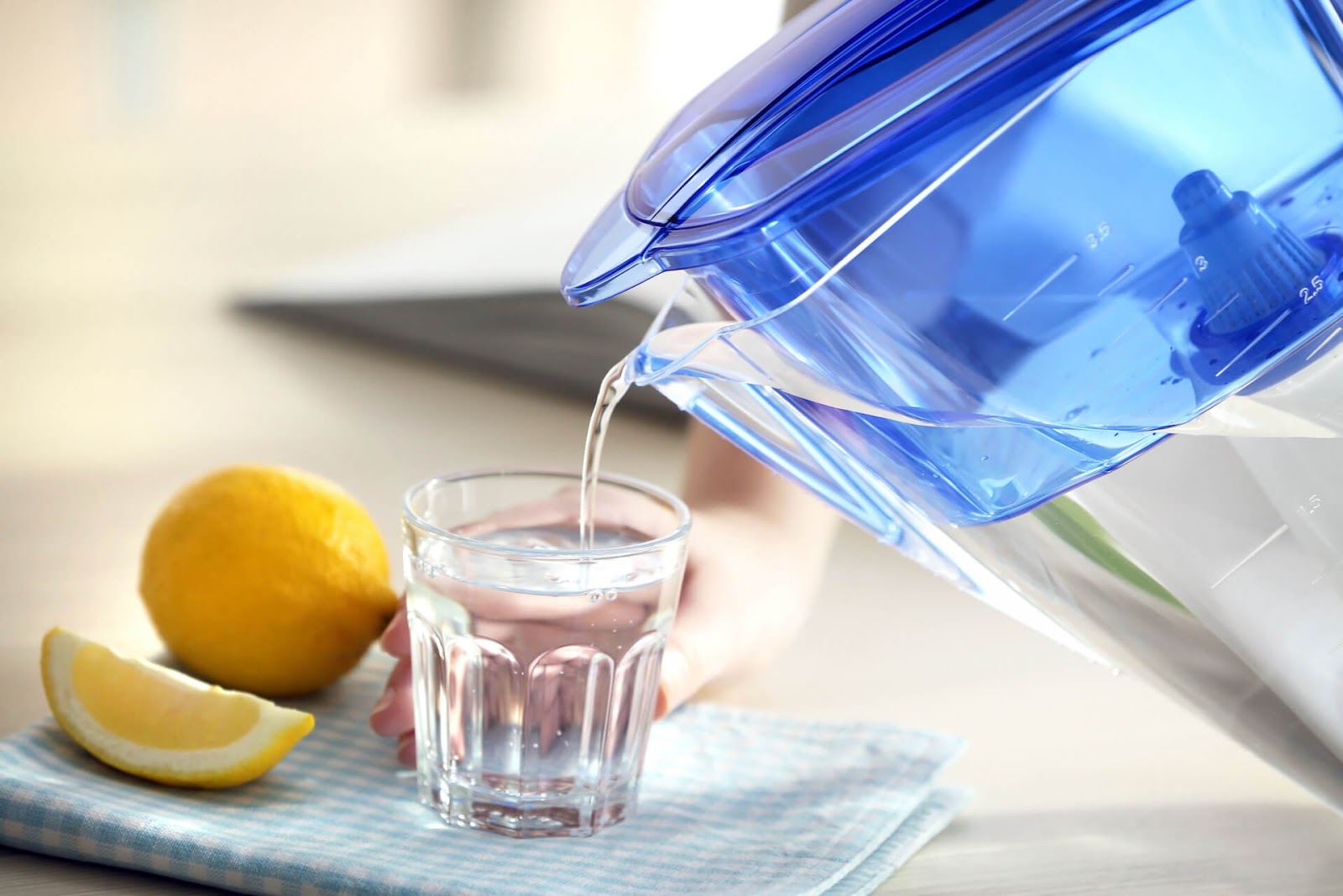 Someone pouring water from a pitcher into a cup with some lingering lemons nearby