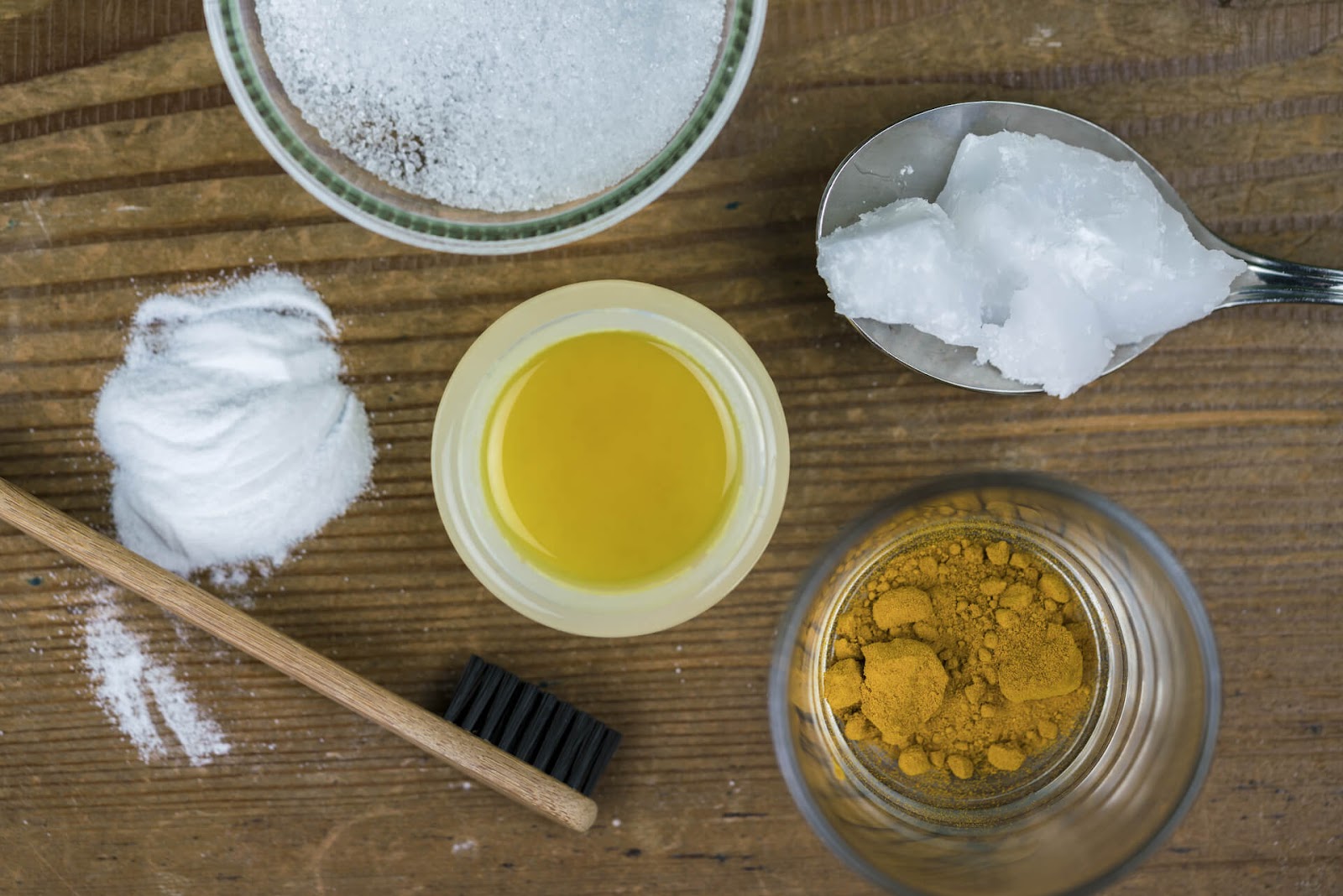 Toothbrush next to jars and spoons of teeth-whitening goodies