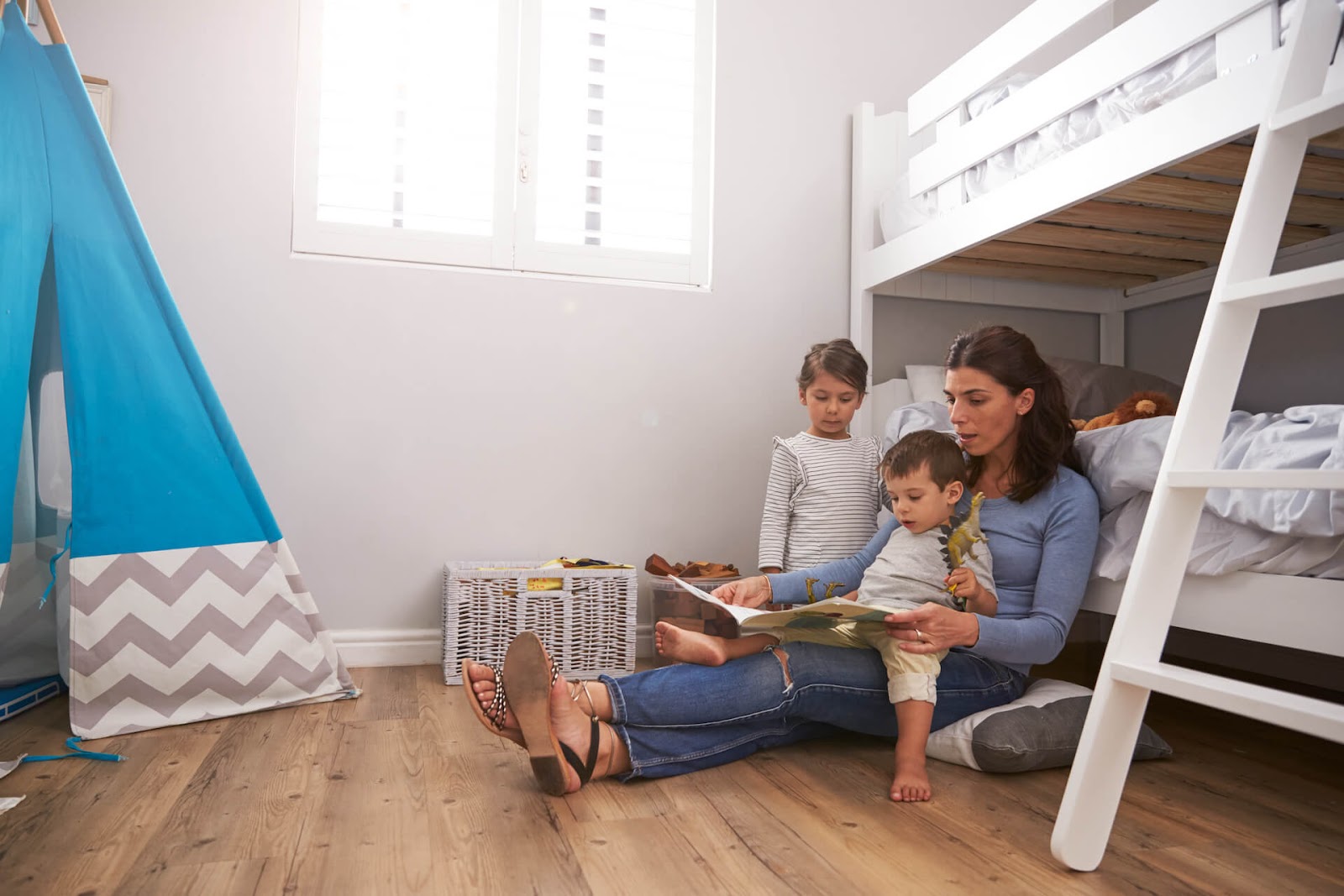 Mom leaning against her children's bunk beds, reading a story to them