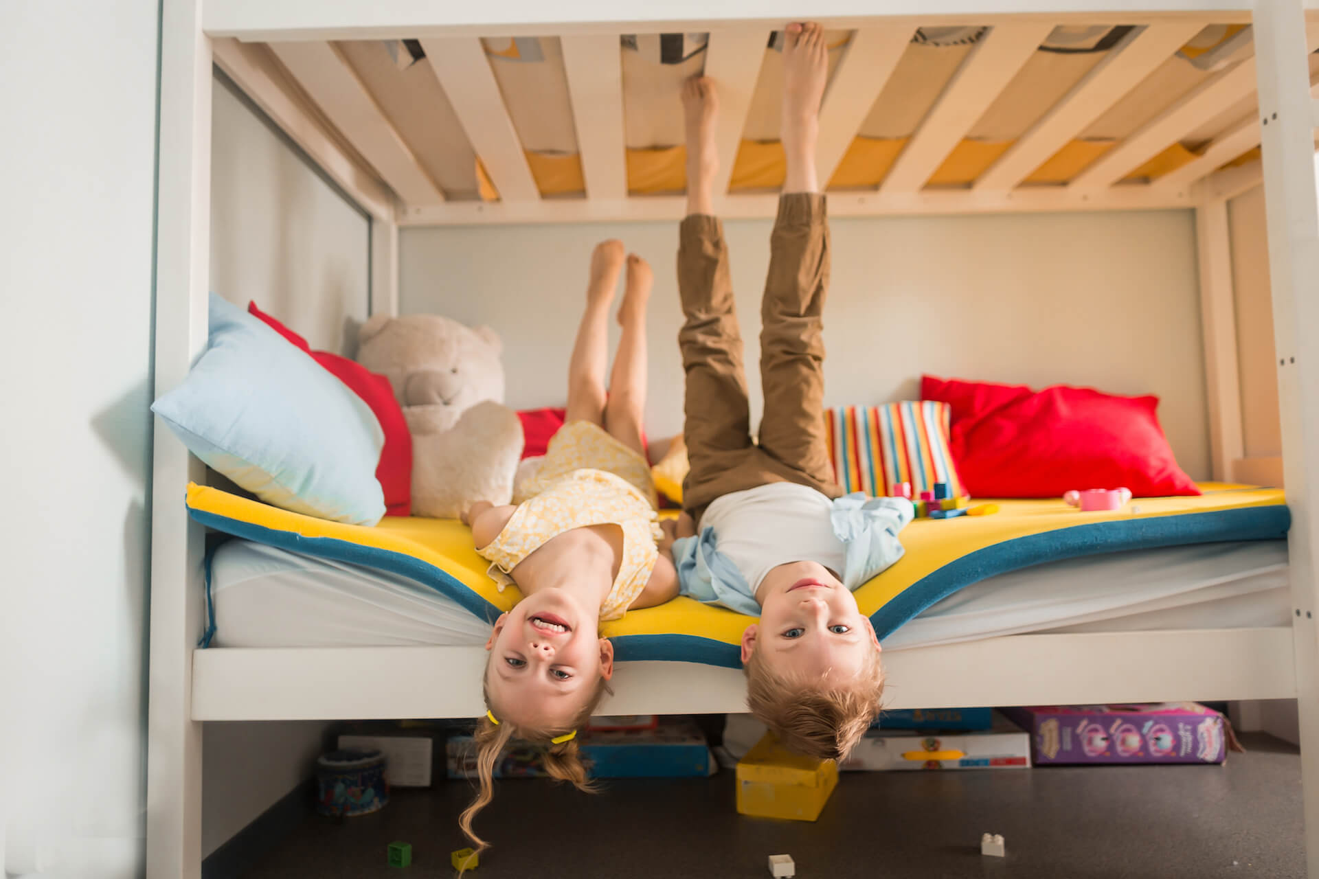 Kids playing on the bottom of a bunk bed, head hanging over and feet in the air