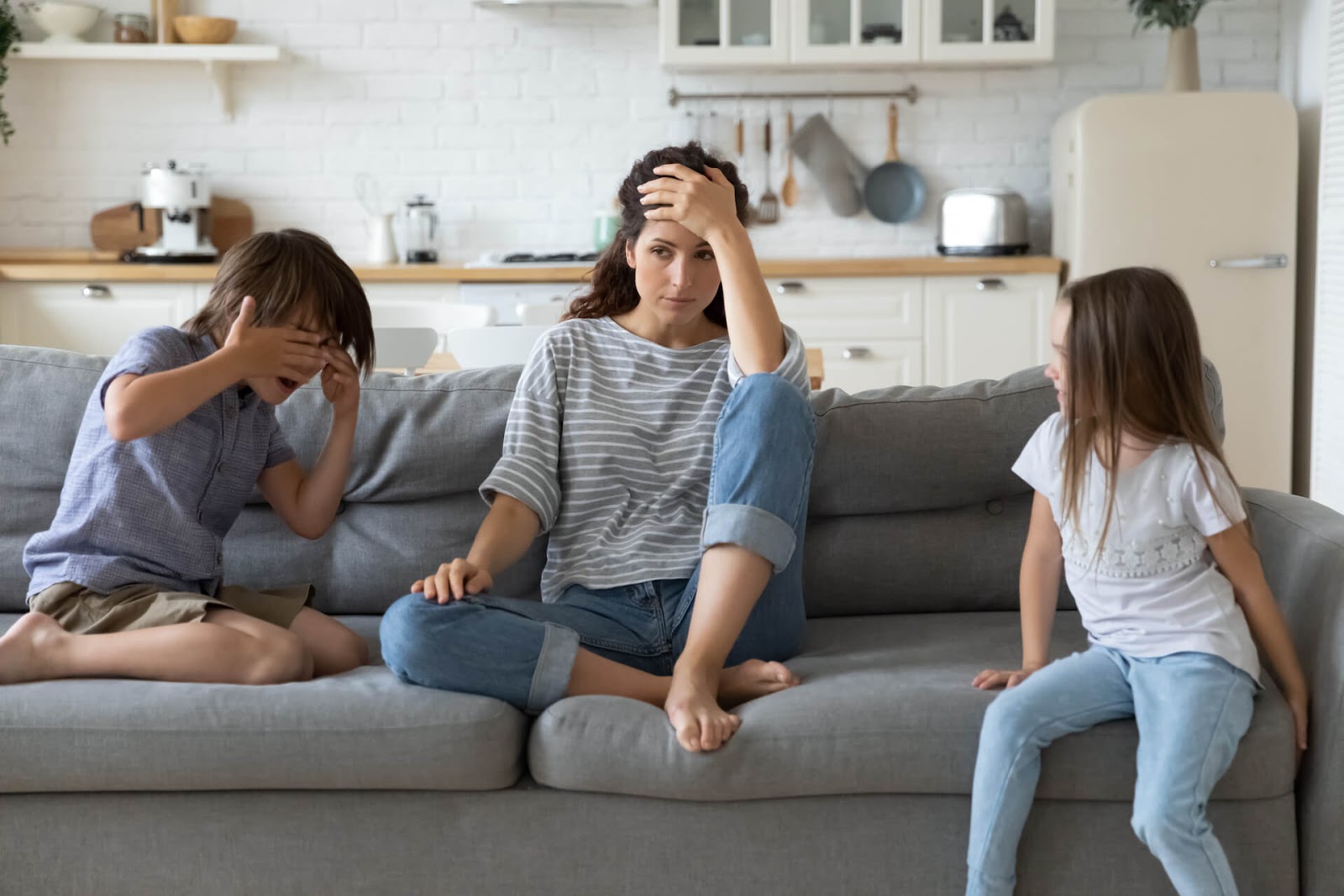 Unhappy mom on couch next to her two children