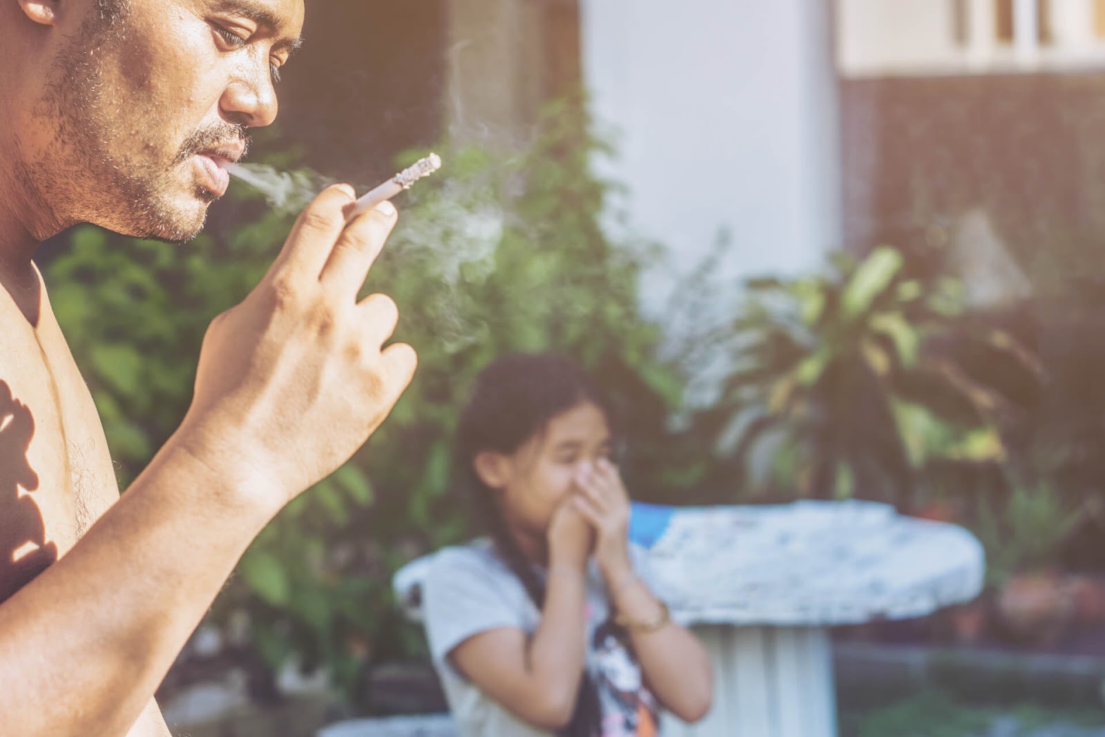 Father smoking a cigarette with daughter in the background
