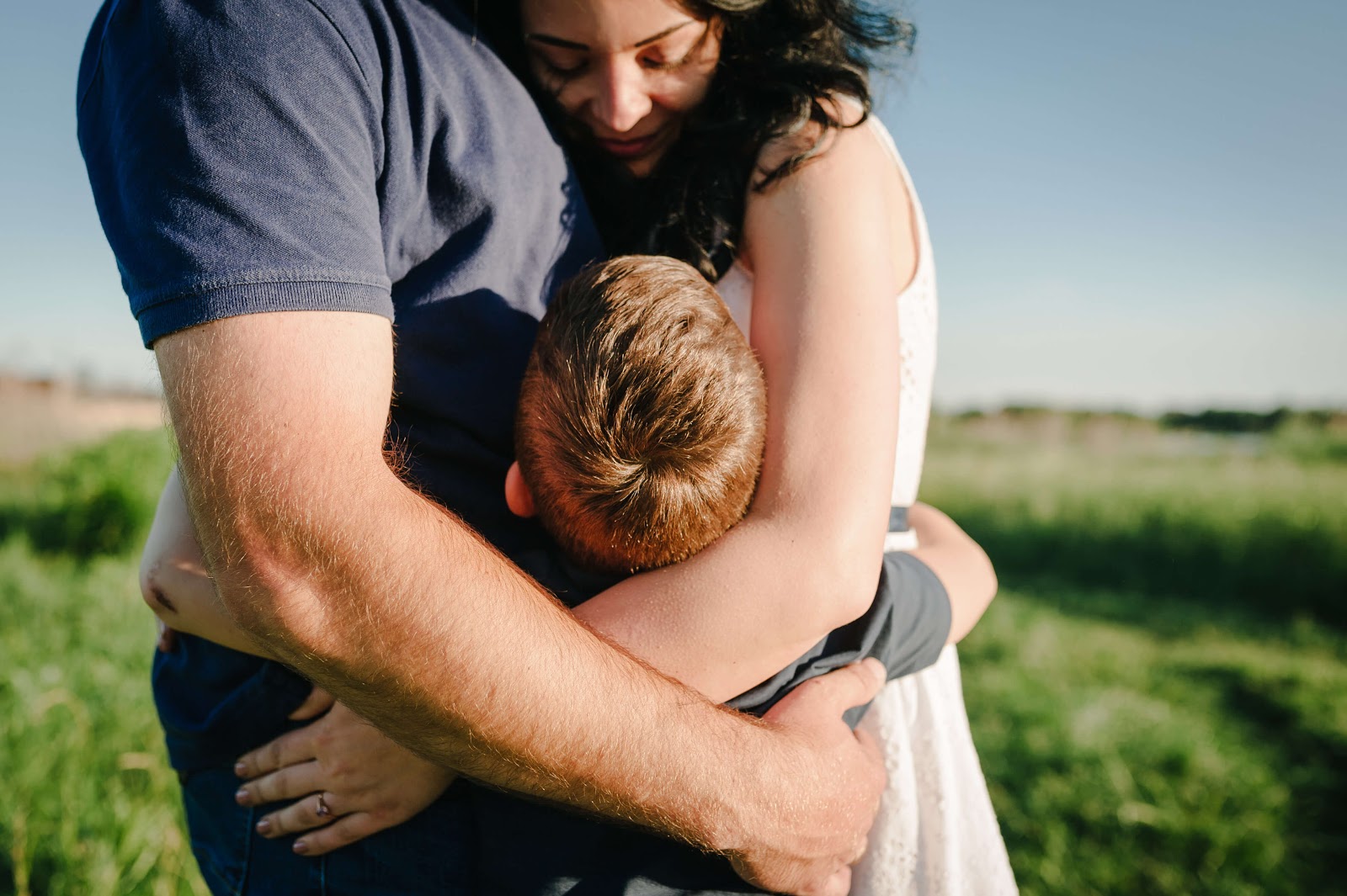 Mom, dad and son group hug in the summer sun
