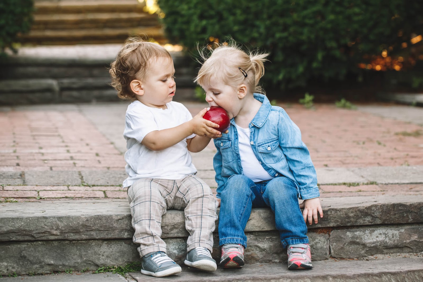 Toddler boy sharing his apple with a girl