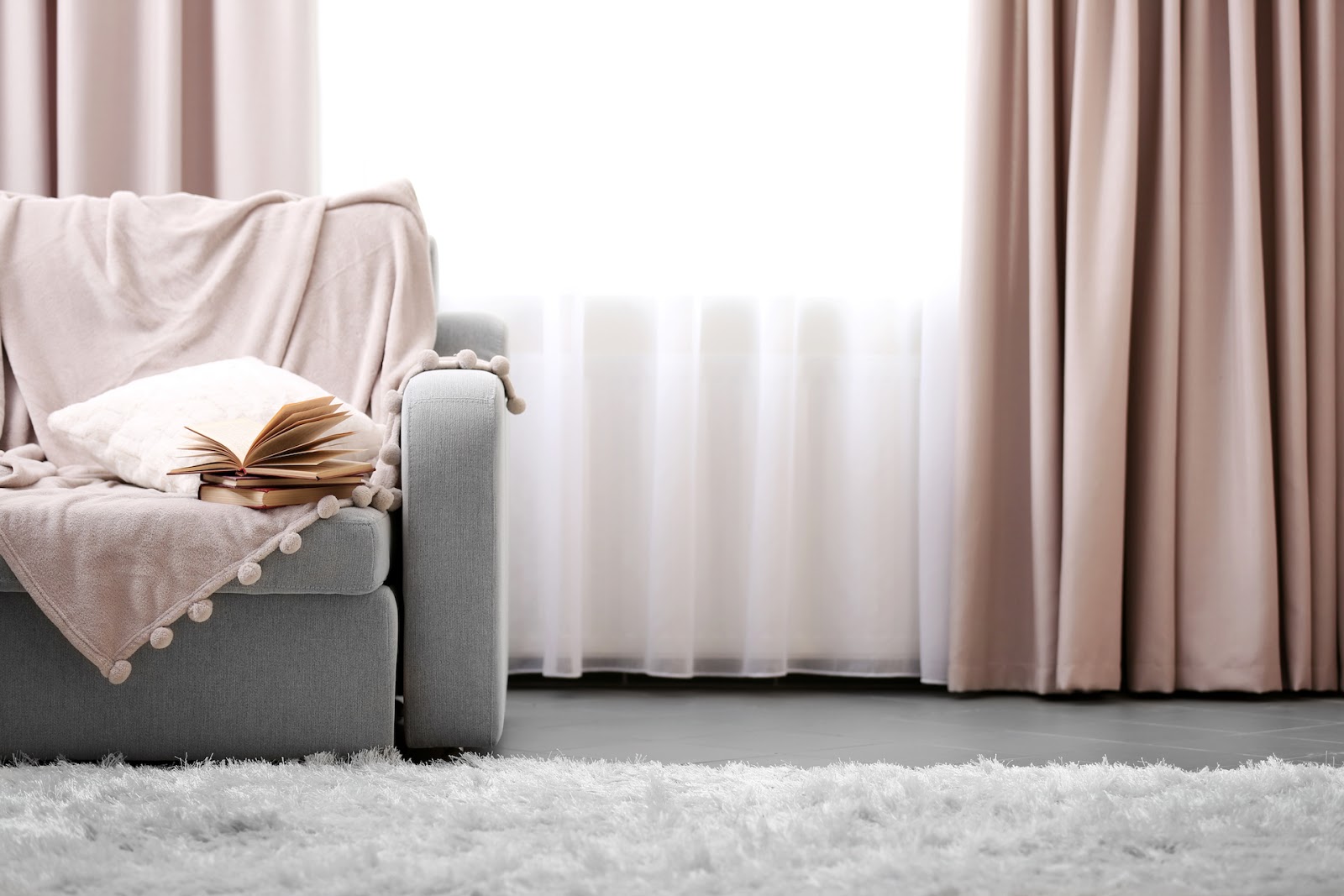 Dusty rose curtains with grey couch and pink blanket draped over itv