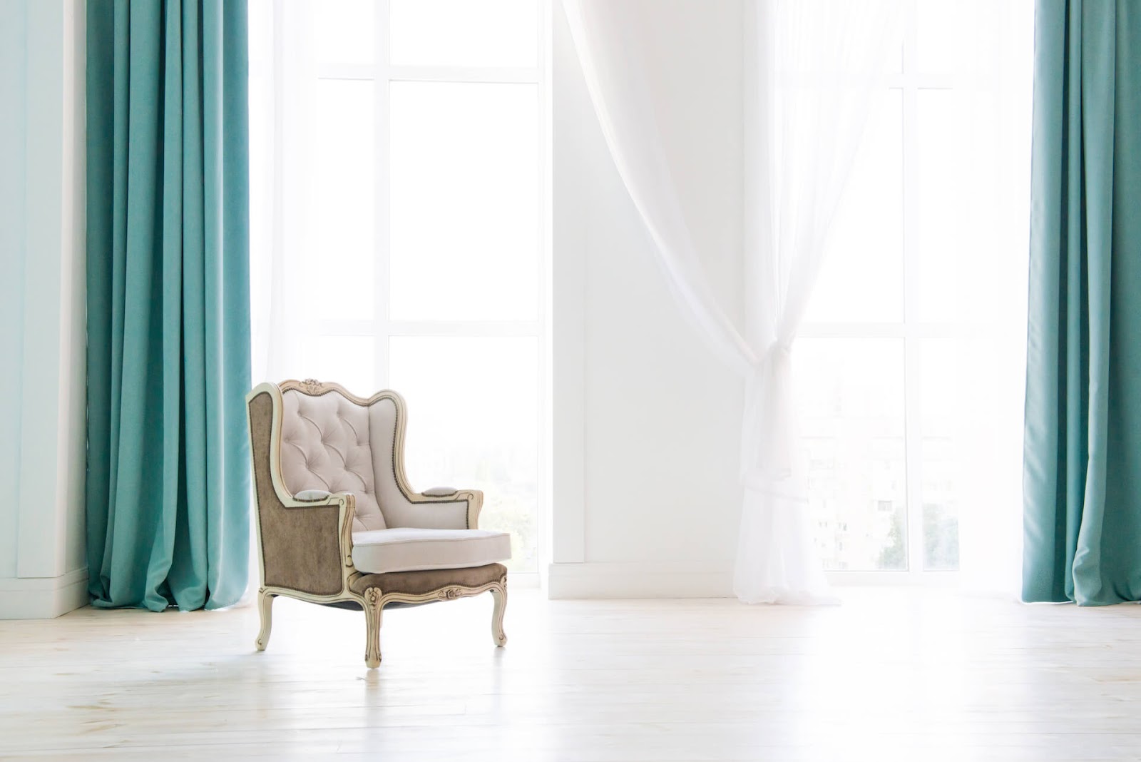 White wingback chair in white room with teal, floor-to-ceiling curtains