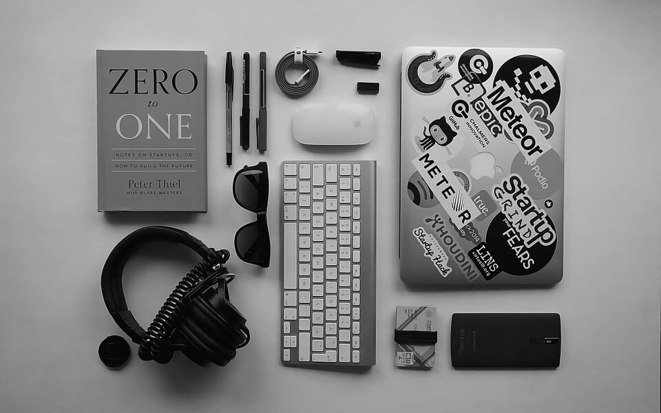 Black and gray college student desk tools including laptop, book, sunglasses, pens, headphones and more