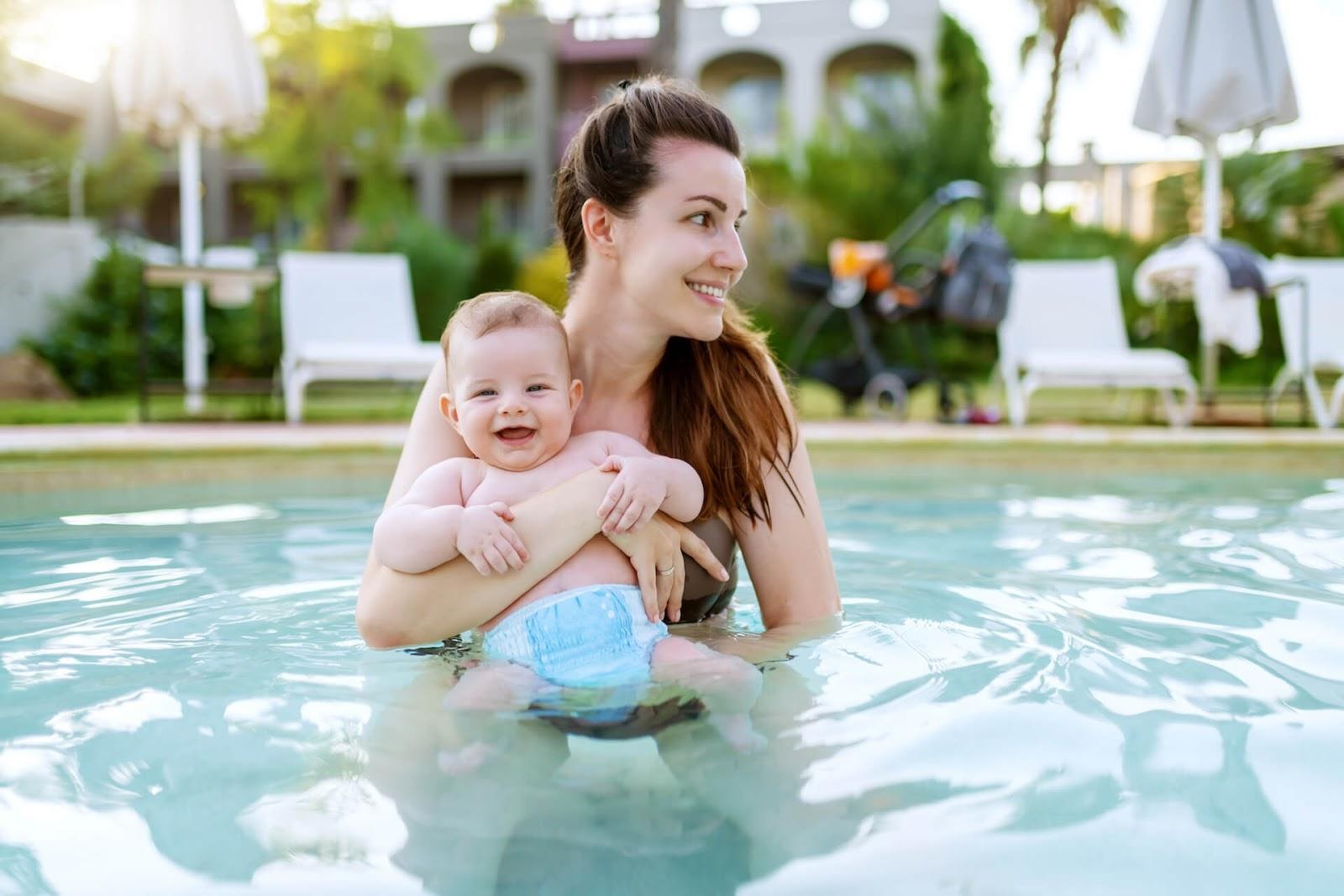 Mom holding young son with swim diapers in a swimming pool