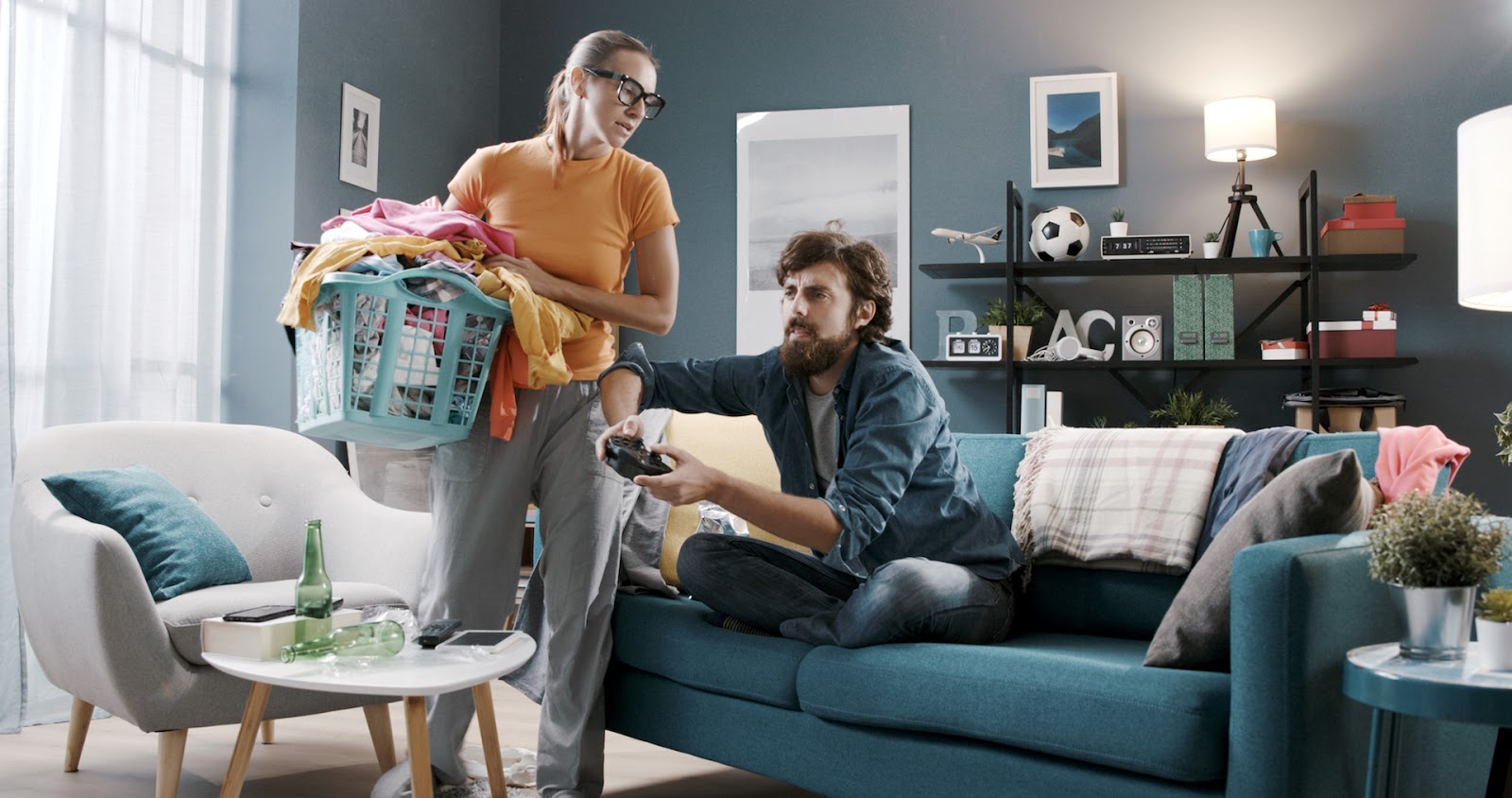 Frustrated woman doing laundry while her husband plays video games