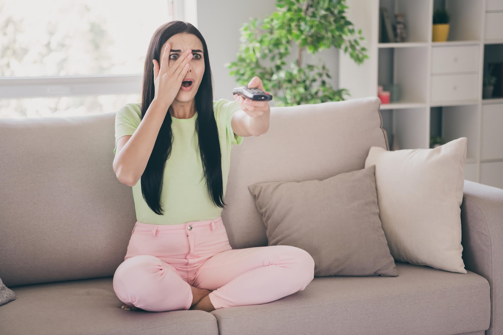 Woman looking horrified at tv while still watching it