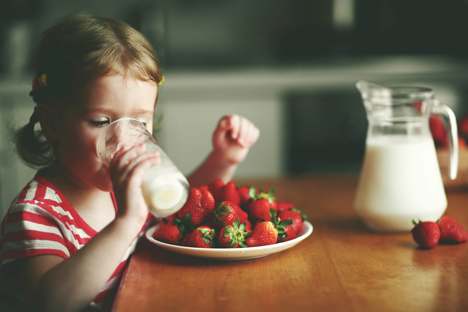 Young girl drinking pea milk with some strawberries nearby