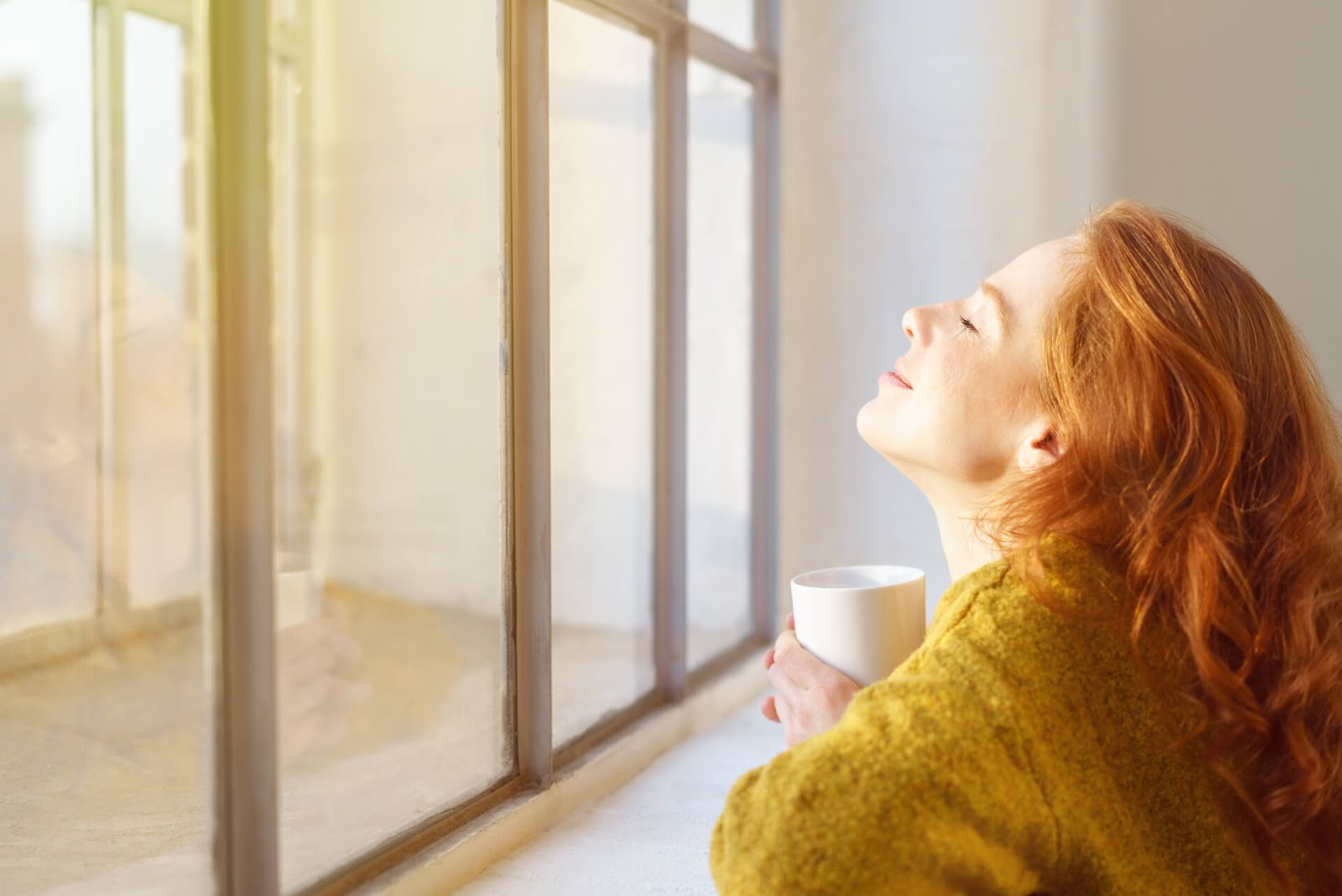 Woman soaking in the sun from her living room with a cup of