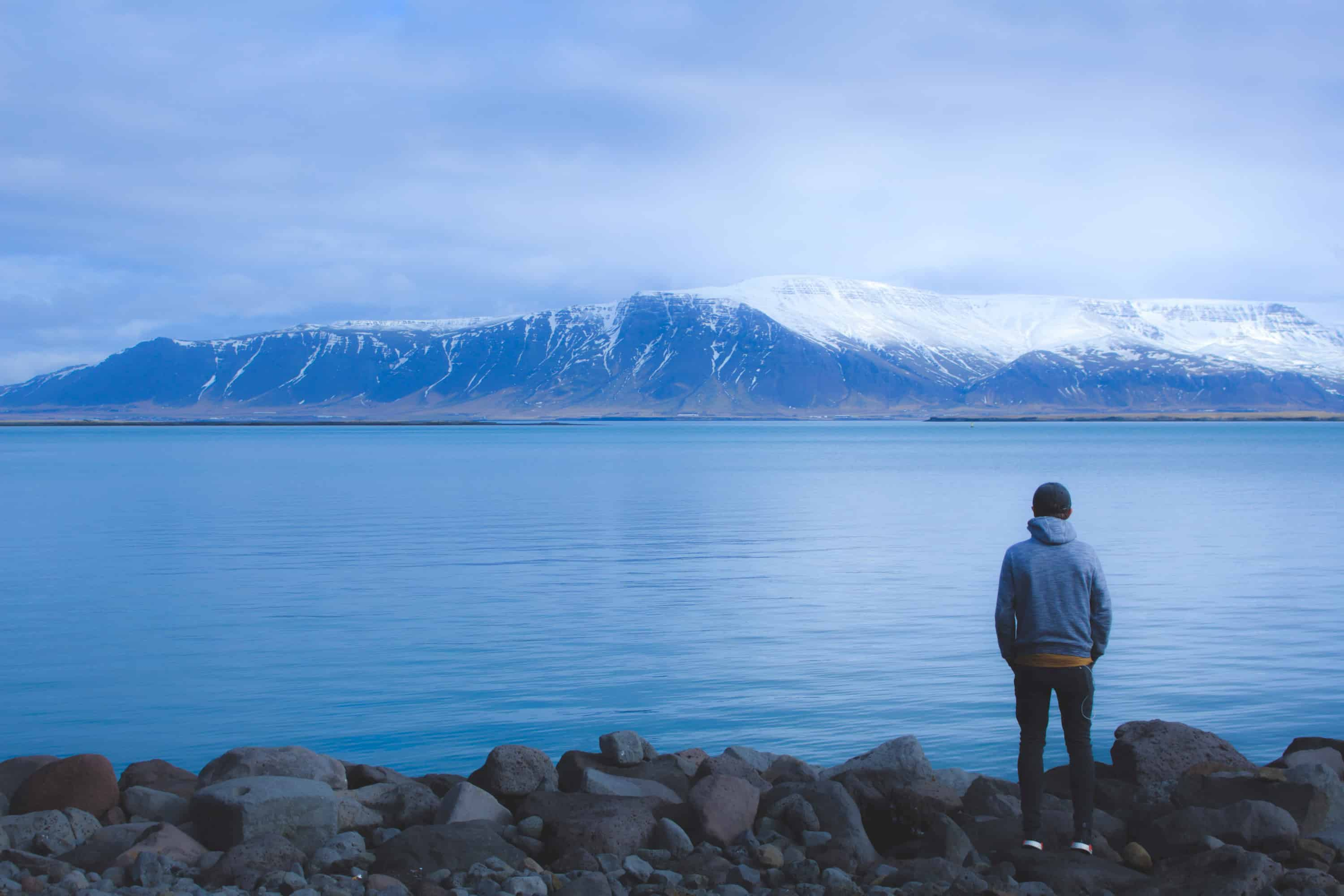 A man facing a mountain range with a lake in front.