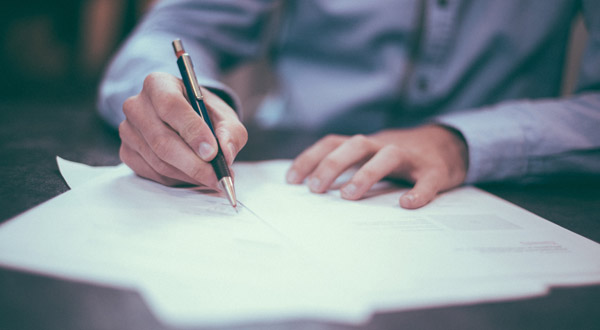 Hands writing on a collection of papers with a pen