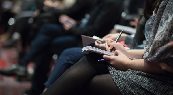 Seated presentation audience members writing in notebooks