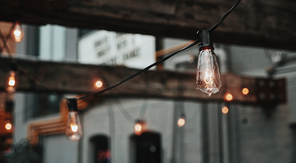 Bare light bulbs hanging from wooden beams in front of grey warehouse