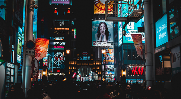 Crowded city square in Osaka, Japan at night with advertisements in the background