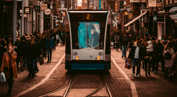 Light rail in the middle of busy street in Amsterdam with pedestrians on either side