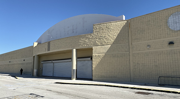 A woman stands next to a shuttered Kmart storefront in an empty parking lot