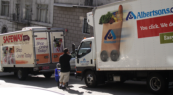 A man stands between two grocery delivery trucks