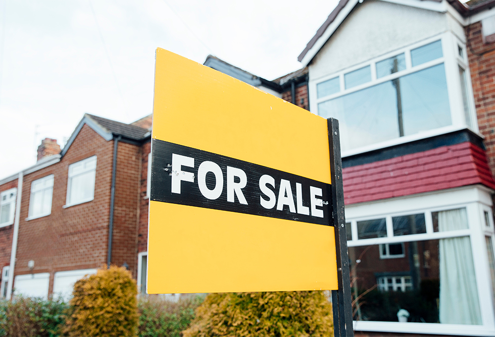 Yellow "for sale" sign in front of two story residences