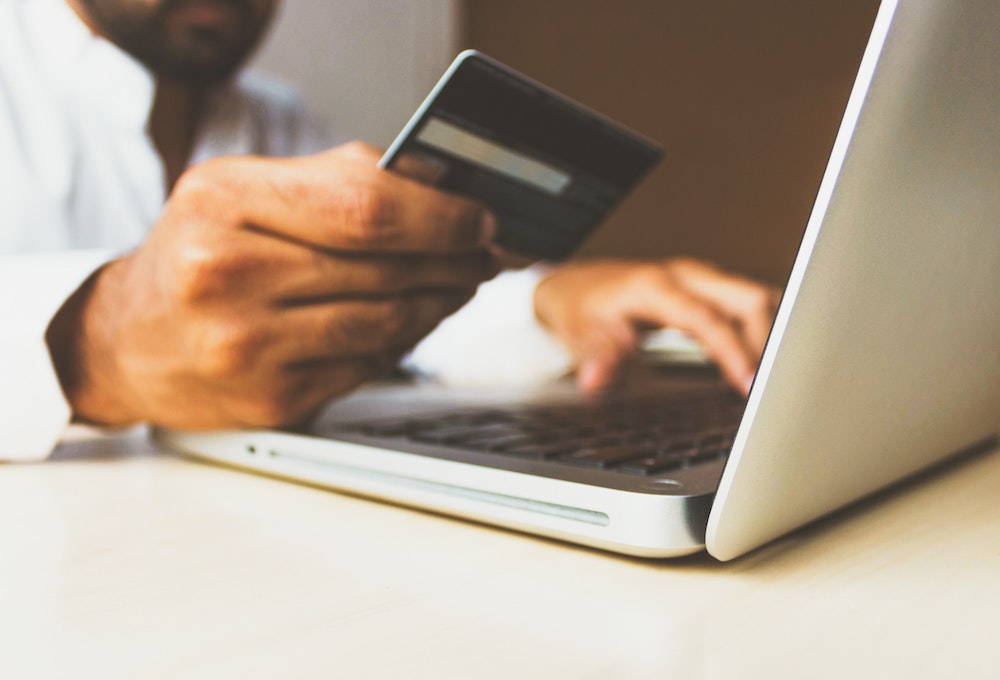 Person holding credit card in one hand and typing with the other hand.