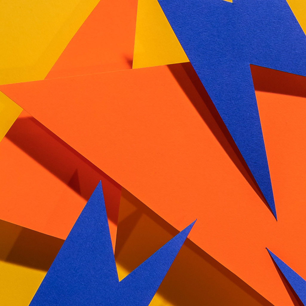 Orange and blue construction paper shapes with sharp angles on bright yellow background