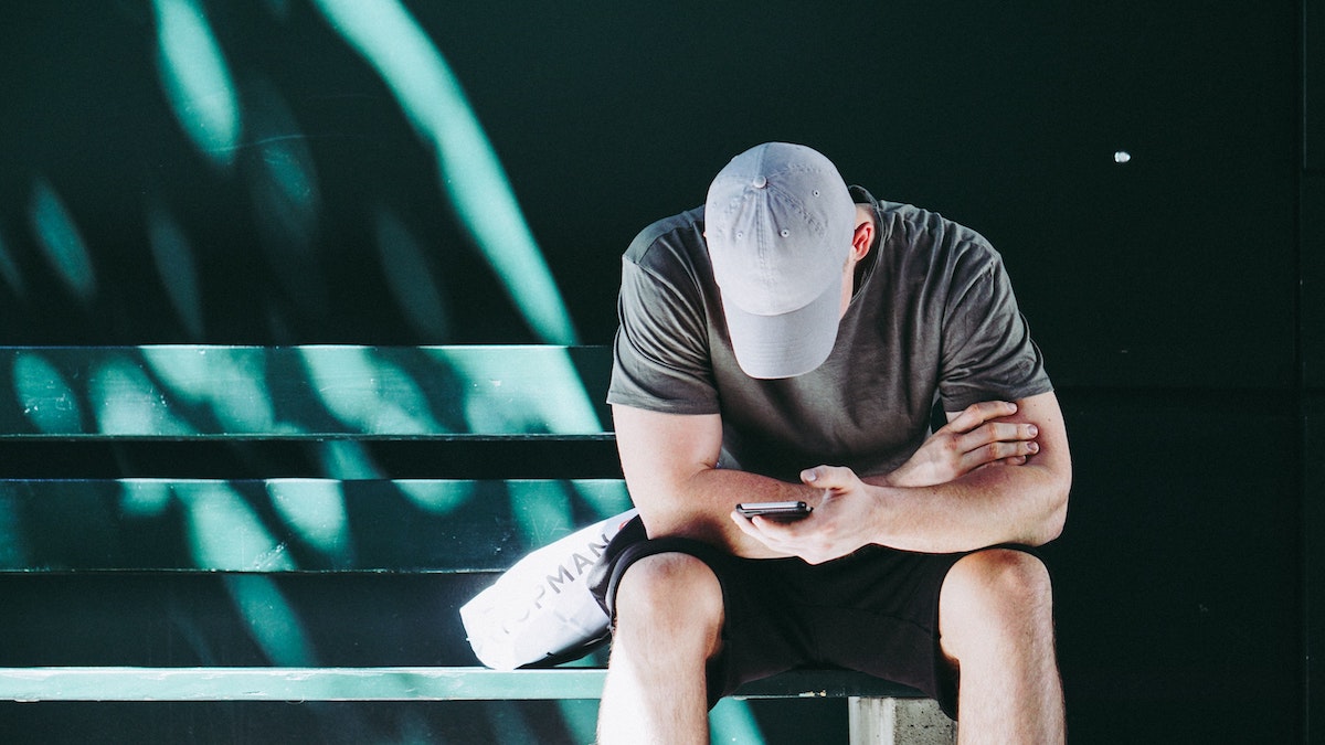 Sitting man in baseball cap using smartphone