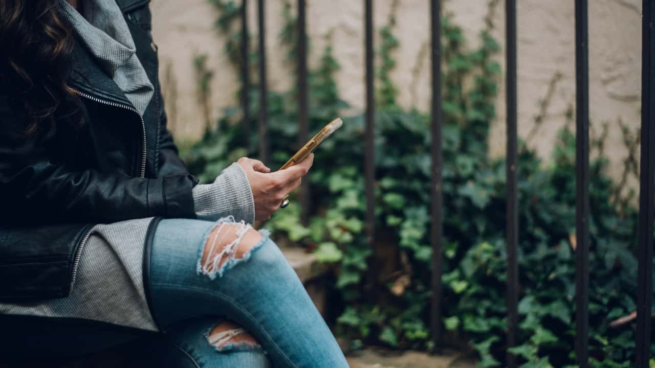Photo of a woman sitting cross-legged on a bench outdoors using her iPhone