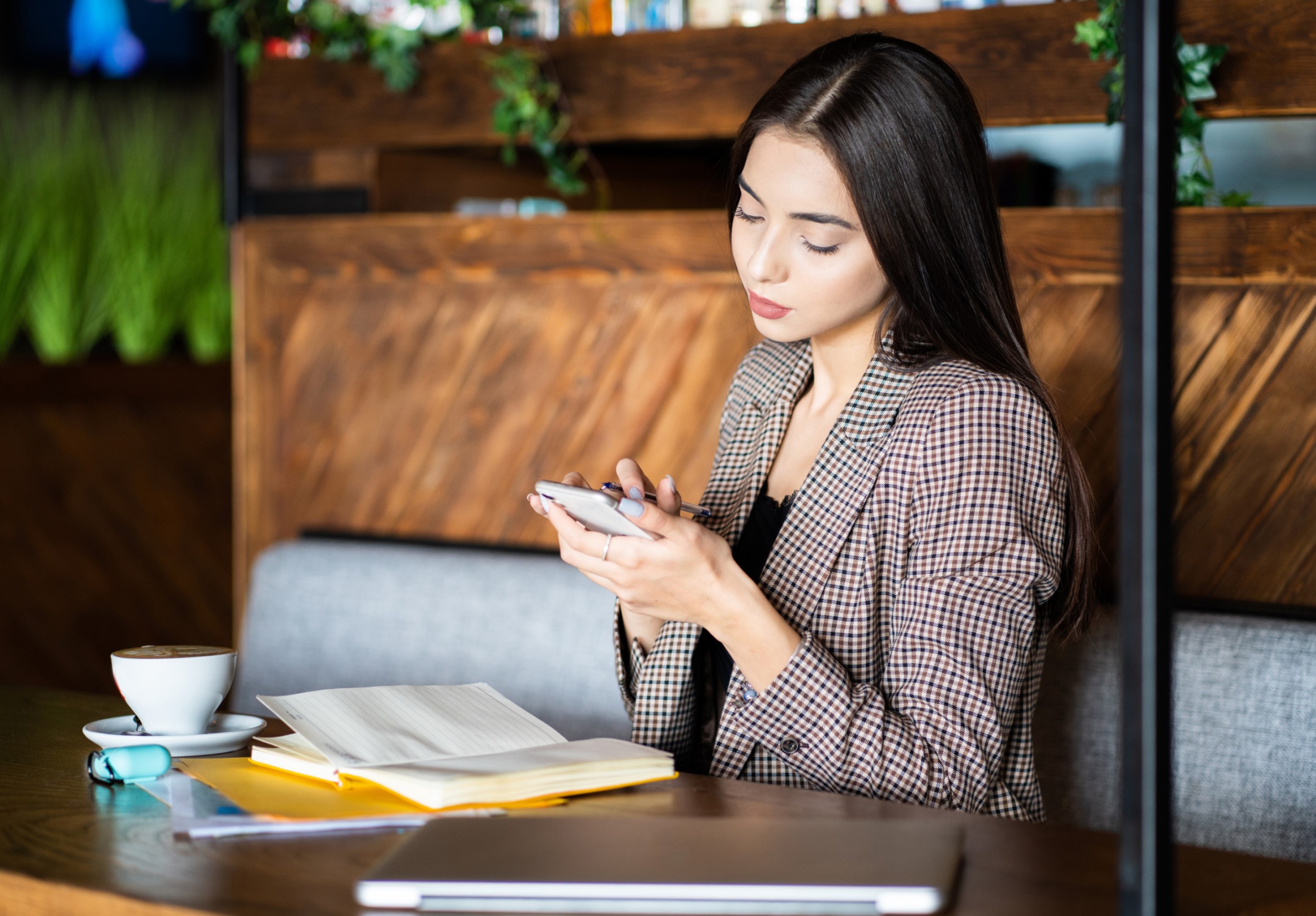 Woman sitting in restaurant booth, reading her phone with a book and coffee on the table