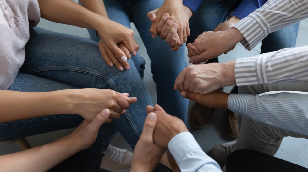 Reforming addicts holding hands at a rehabilitation meeting. 