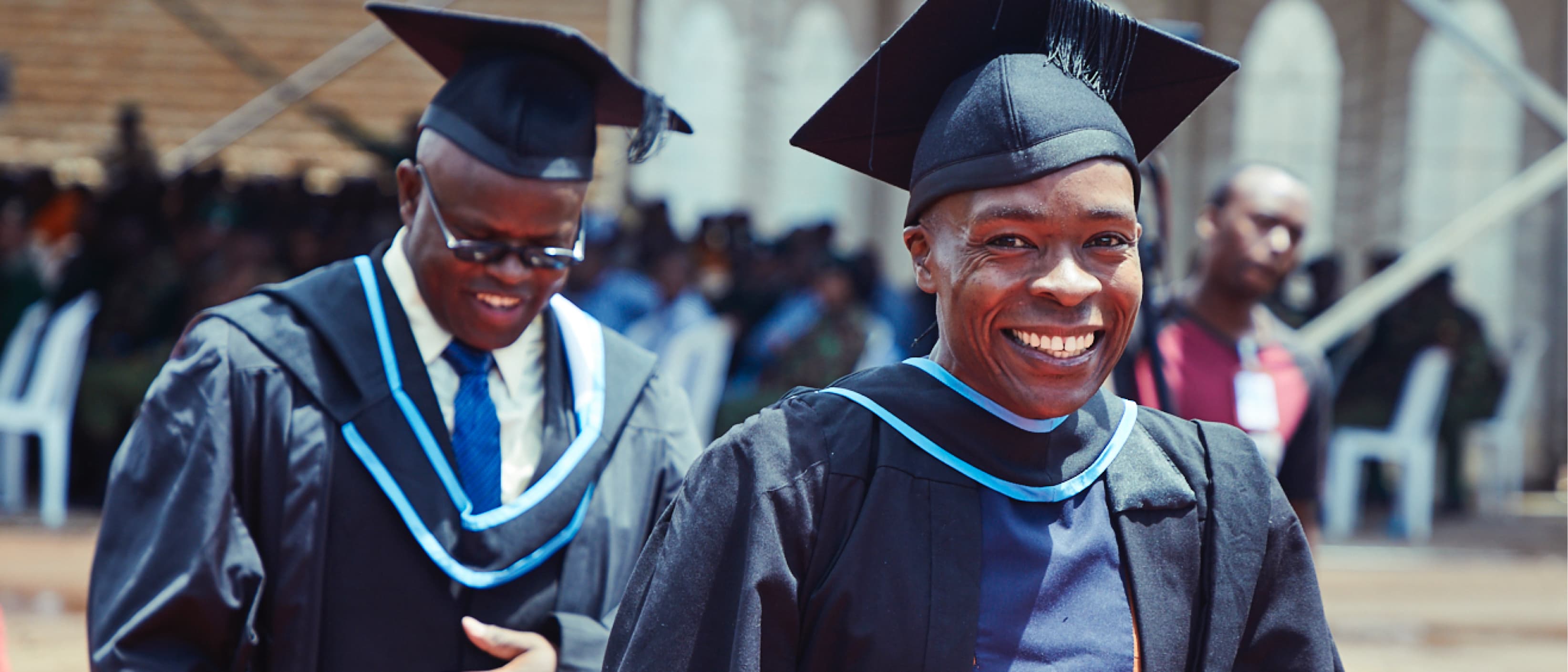 Two Justice Defenders graduates smile while wearing their robes and caps.