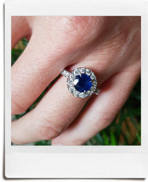 Round blue sapphire set within 12 round brilliant diamonds making cluster engagement ring