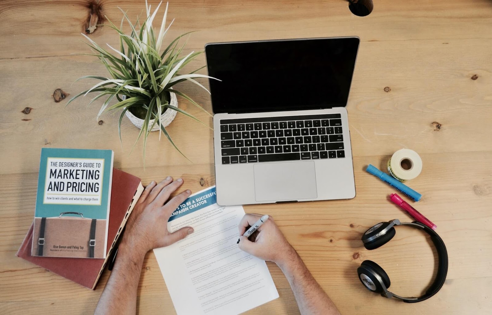 desk with laptop, books, papers, and pens on top