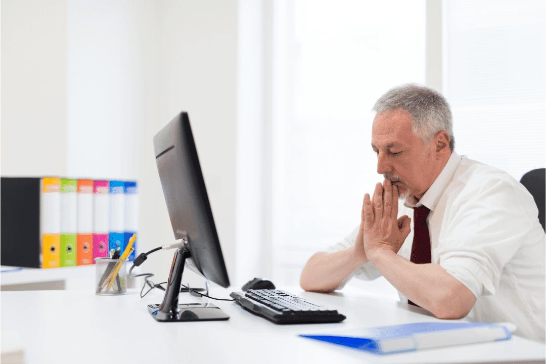 older man looking frustrated while looking at computer screen in office