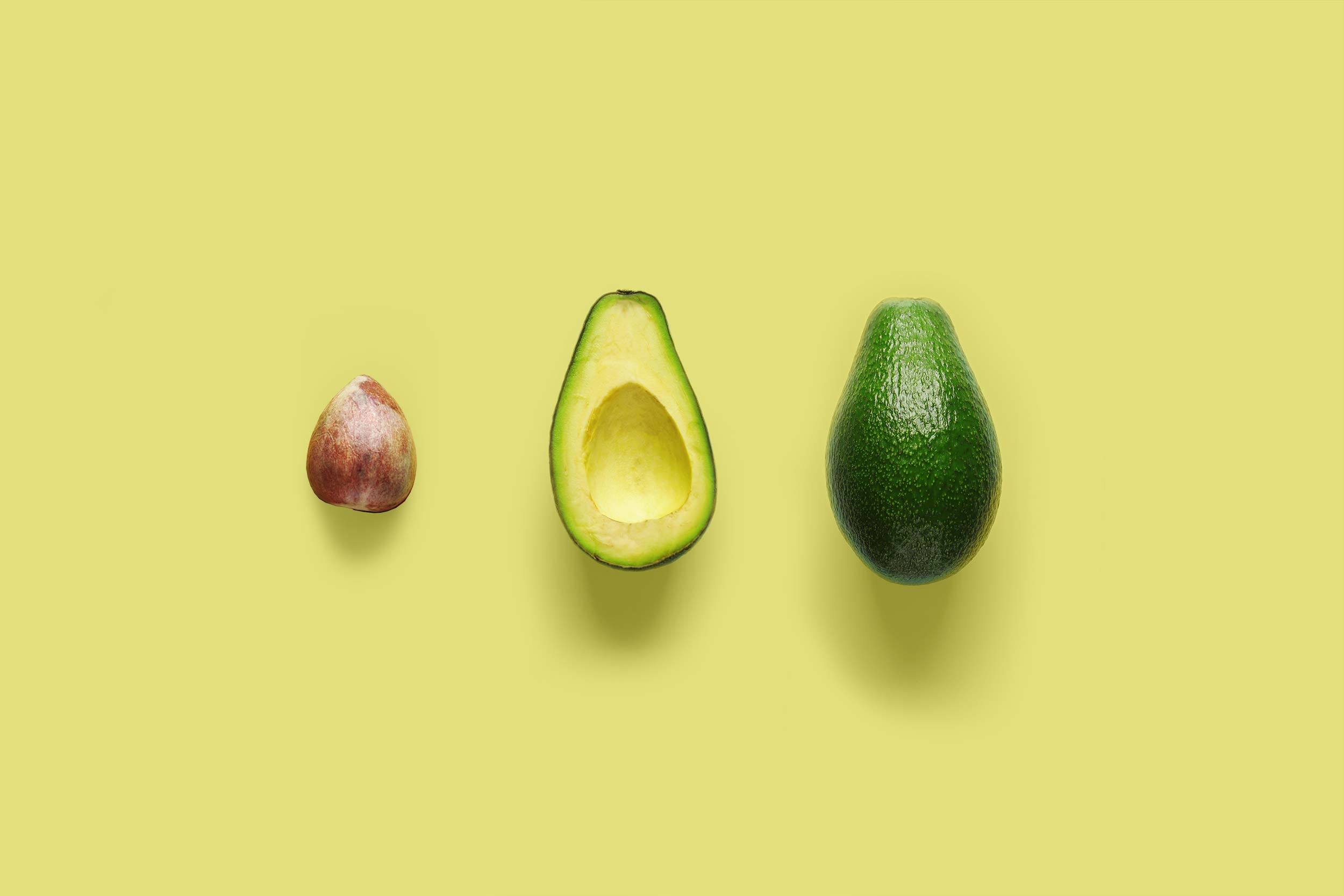 The seed of an avocado, the flesh in the skin of an avocado and a whole avocado
