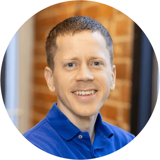 white man with short and straight strawberry blonde hair with a large smile wearing a blue shirt