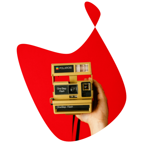 Hand holding a yellow polaroid camera on a red background. 