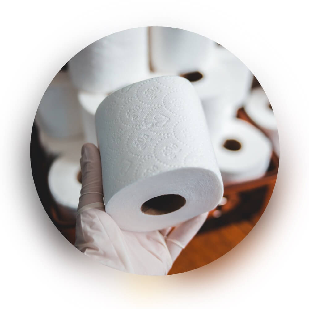  Hand in a glove holding a roll of toilet paper with more rolls in the background