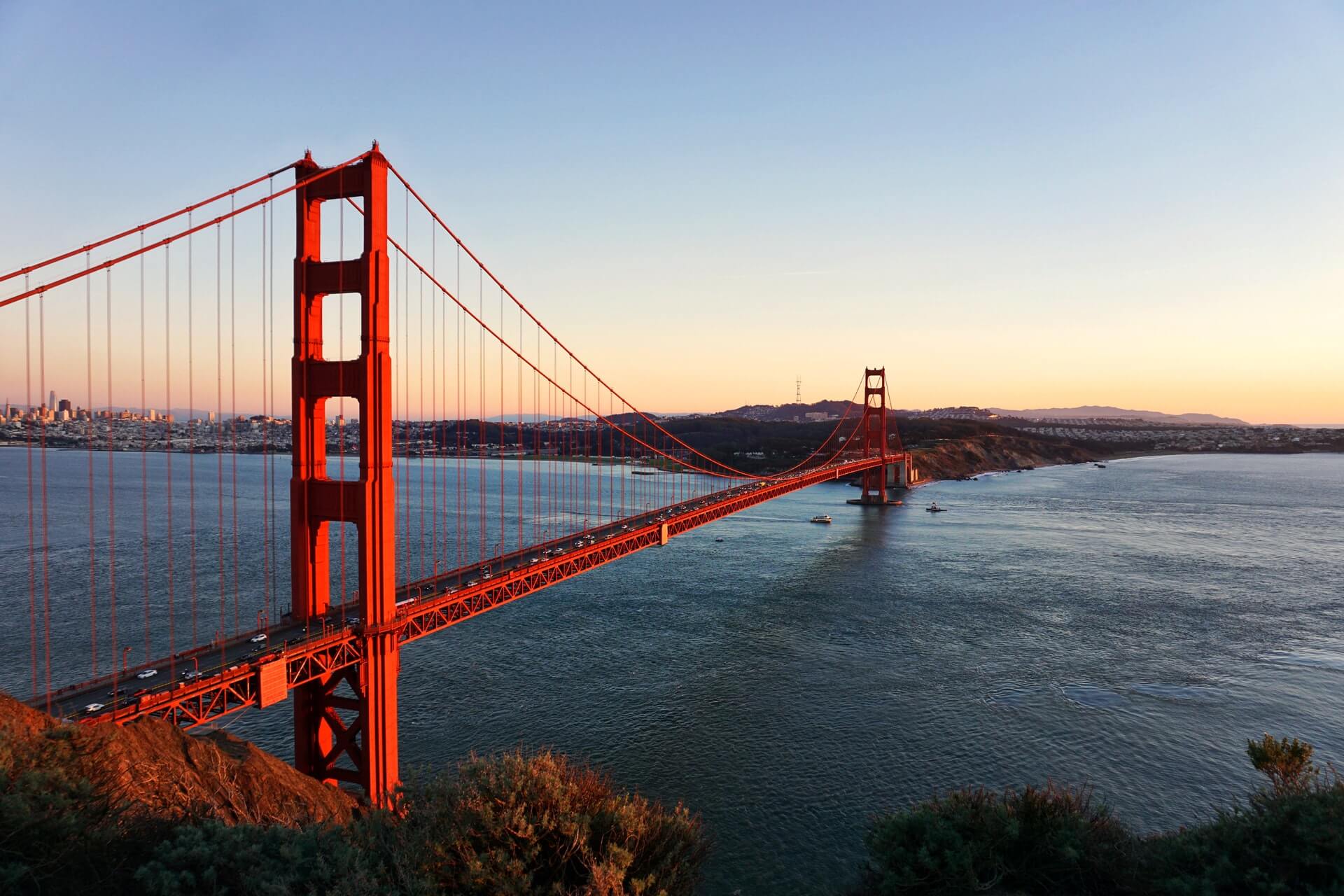 The Golden Gate Bridge at sunset with clear skies and calm waters below