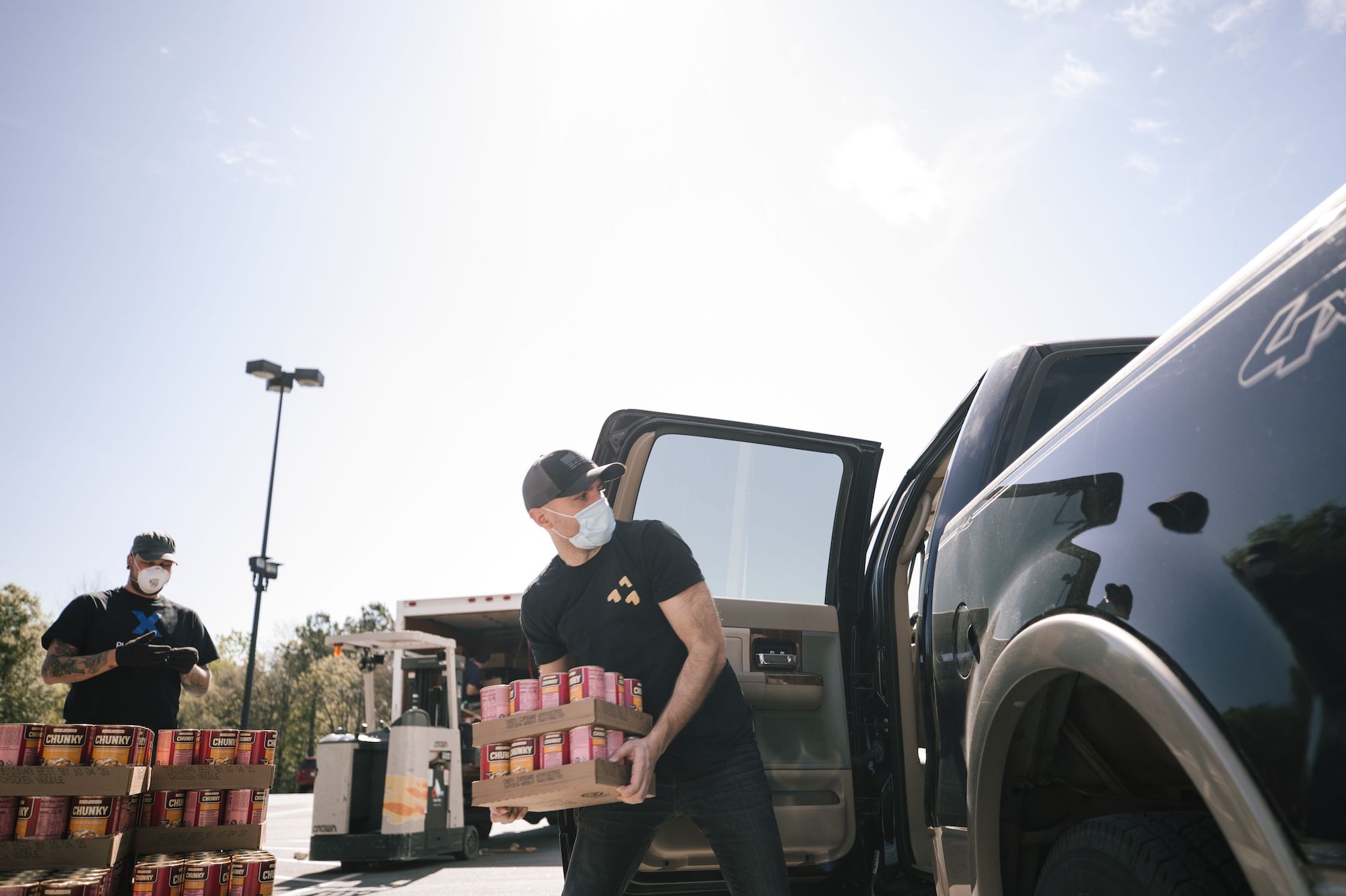 A man unloads canned goods from a truck while wearing a mask.