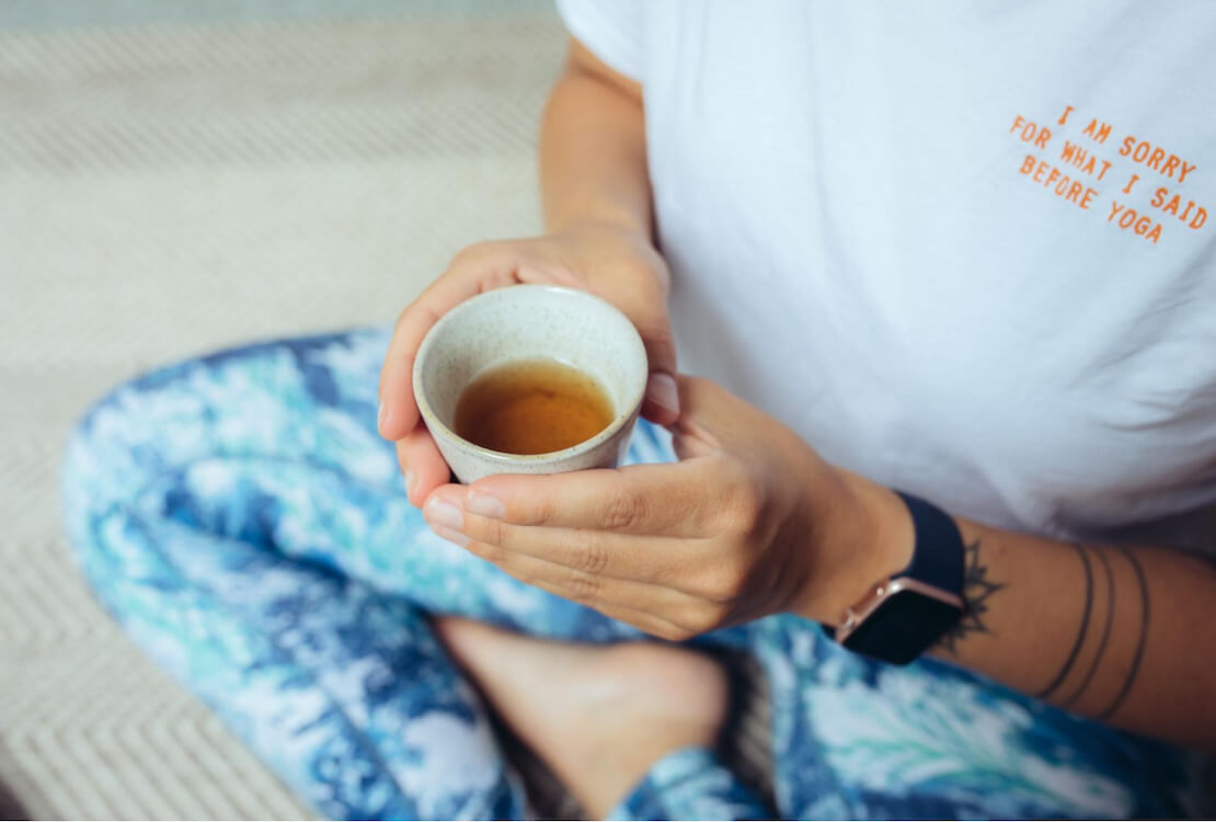 A person holding a cup of tea, wearing a t-shirt that says "I'm sorry for what I said before yoga"