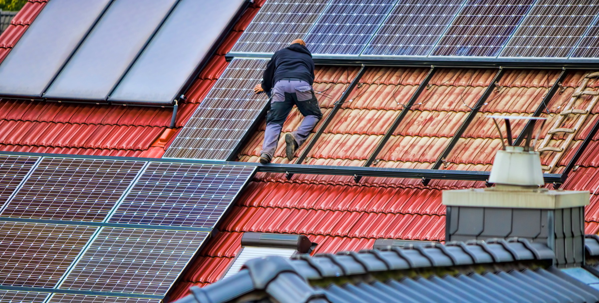 Ein Handwerker auf einem roten Dach, der eine Photovoltaikanlage installiert